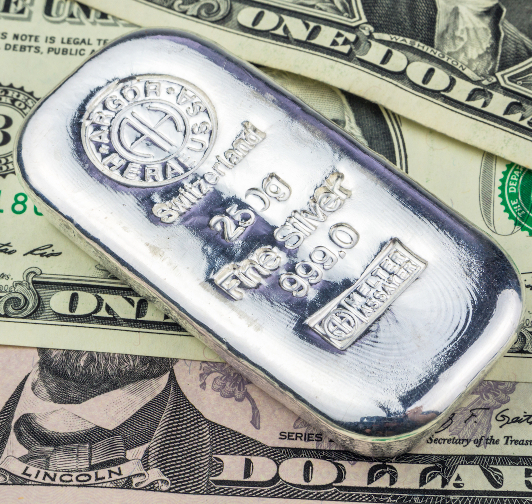silver brick laying on dollar banknotes
